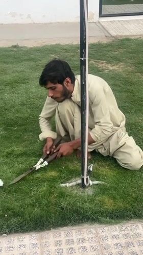 Man trims grass with shears in Quetta City
