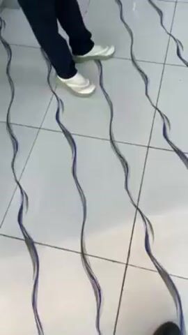 A person wearing dark pants and light-colored shoes stands on a white tiled floor with wavy blue and gray lines. The camera is positioned above the person's feet, looking down at the floor. The person remains still.