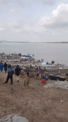 Waterfront marketplace bustling with boats, traders, and sacked goods