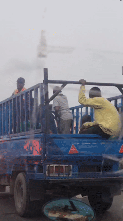 Blue cage truck moves through Lagos traffic during overcast day