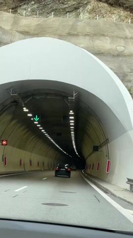 The video shows a car driving through a tunnel. The tunnel is well-lit with lights along the ceiling. There are green directional signs and a speed limit sign showing 80. Other cars are visible ahead. The road is asphalt, marked with white lines. The walls of the tunnel are grey concrete.