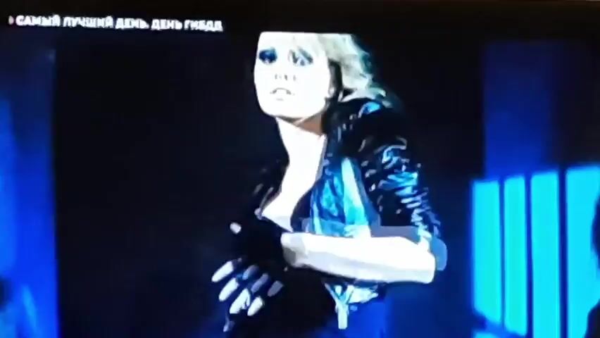 The video opens with a close-up of a woman with blonde hair, wearing dark clothing and a black leather jacket. She is looking directly at the camera with dramatic eye makeup. The scene is dimly lit with blue light. The video then cuts to a close-up of another woman with dark, curly hair, also looking at the camera. This is followed by a close-up of a man wearing a police-style hat and uniform. The video then shows two women, one with blonde hair and the other with dark hair, separated by what appear to be metal bars, resembling a jail cell. Both women are looking down. The text "САМЫЙ ЛУЧШИЙ ДЕНЬ. ДЕНЬ ГИБДД" appears at the top of the screen in white text against a black background, which translates to "BEST DAY. TRAFFIC POLICE DAY."