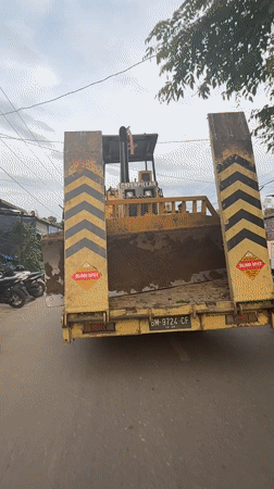 Heavy machinery transported through Indonesian villages on flatbed trailer