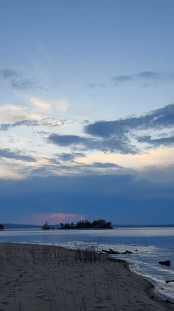 Three people watch sunset at Vekoshinka beach in Russia
