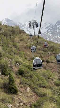 Colorful gondolas carry passengers up green mountainside near Almaty