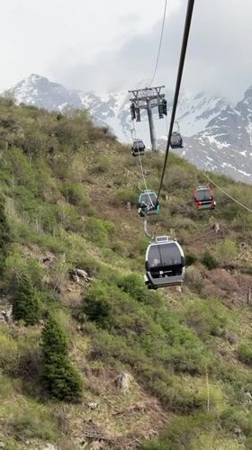 Colorful gondolas carry passengers up green mountainside near Almaty