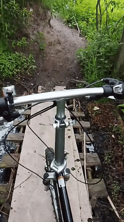 Cyclist crosses wooden bridge over stream in Russian woods