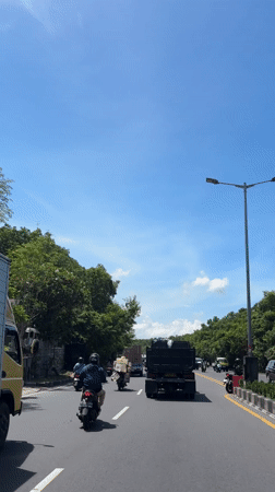 Sunny morning traffic observed on tree-lined Kuta road