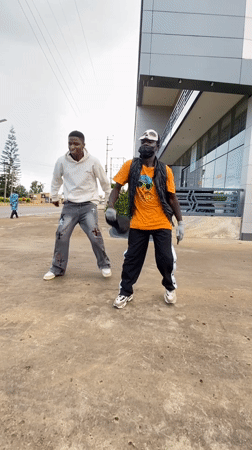 Masked duo dances outside a modern building in Bukuru
