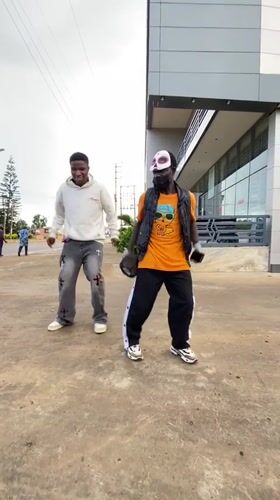 Masked duo dances outside a modern building in Bukuru