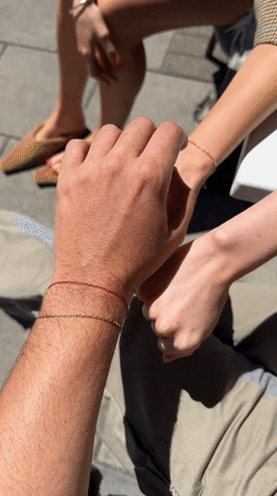 Hands meeting outdoors in London, red bracelet in frame