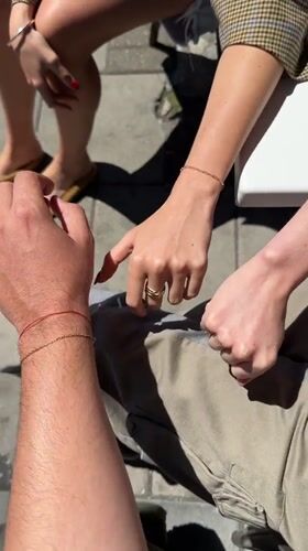 Hands meeting outdoors in London, red bracelet in frame