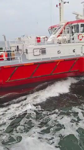 The video shows a red and white pilot boat, labeled "PILOT", moving through the water. The boat is creating a noticeable wake. The sky is overcast and the water appears somewhat choppy.  There are some white structures on the upper deck of the boat, including what appears to be antennas.