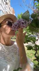 Woman enjoys spring morning in park, smells lilacs, takes selfie