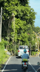 Two motorcyclists travel narrow road in Mengwi, Indonesia