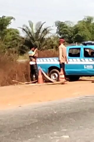 The video shows two men standing near a blue and white truck on the side of a road, with orange cones nearby. A large red tanker truck then passes by. The tanker truck is marked with the name "MINJIBIR" on its rear.