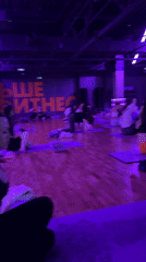 Yoga class with fifteen participants in purple-lit Murino studio