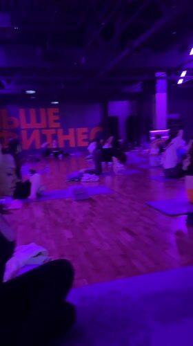 Yoga class with fifteen participants in purple-lit Murino studio