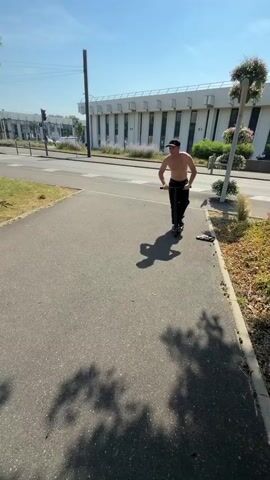 This media file shows a shirtless young man wearing a black baseball cap and black pants riding a black scooter. The video begins with the man riding the scooter on an asphalt path next to a road with a sidewalk and some greenery. In the background, there are buildings and trees. The sun is bright, suggesting it is daytime, and the sky is blue, indicating good weather.

The scene then shifts to the man riding the scooter up a set of concrete stairs. He is moving quickly and appears determined. The setting is outdoors, with more greenery and a railing alongside the stairs. The camera angle is dynamic, following the man as he navigates the stairs. The overall impression is of an athletic individual performing a stunt or practicing a skill on a scooter. There is no visible text in the media file.