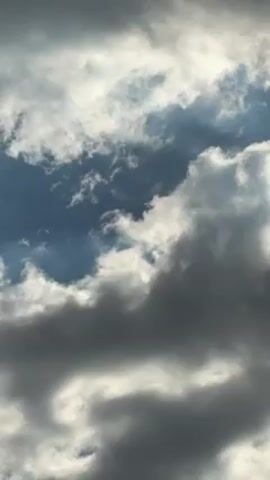 The video shows a cloudy sky with patches of blue. Some clouds are dark gray, while others are white and fluffy. There is movement in the clouds.