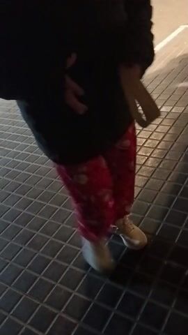 The video shows a person wearing a dark coat and a red bag, who is initially partially visible. The camera then focuses on the dark gray tiled floor, panning slightly across it, revealing the square tile pattern. There is some light reflecting on the tiles.