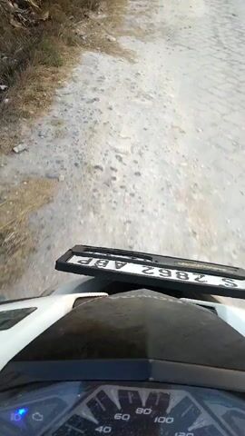 The video shows a first-person perspective of someone riding a motorcycle on a dirt road. The license plate of the motorcycle is visible, displaying the characters S 2862 ABP. The camera then pans to the left, revealing a rural landscape with green fields and banana trees. The sun is setting, casting a warm glow across the sky. The scene is peaceful and serene.