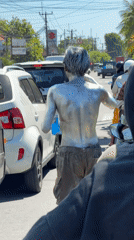 Silver-painted street performer interacts with traffic in Denpasar