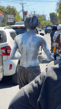 Silver-painted street performer interacts with traffic in Denpasar