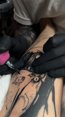 Person receives lower leg tattoo from gloved artist