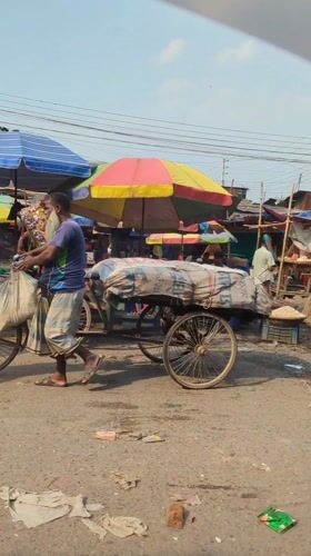 Man pushes tricycle cart through Dhaka marketplace