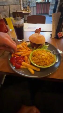 The video shows a table in a restaurant, laid out with a meal consisting of a burger, french fries, and rice. There are also drinks and condiments on the table. A waiter walks up to the table, carrying a tray with more food. Two other people are walking in the background. The restaurant has a casual decor, with wooden walls and tables. The video is shot from a first-person perspective.
