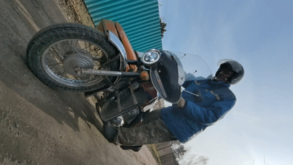 Man starts vintage motorcycle with sidecar on Russian dirt road