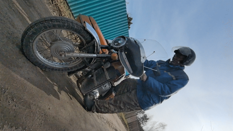 Man starts vintage motorcycle with sidecar on Russian dirt road