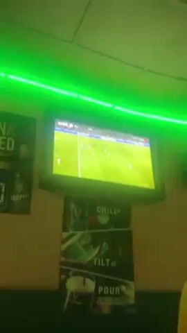 A person is watching a soccer game on TV in a room lit with green LED lights. The game is between Tottenham and Manchester City. The score is 2-0 in the 72nd minute. There is a Guinness advertisement on the wall below the TV. The video is shot from below, looking up at the TV.
