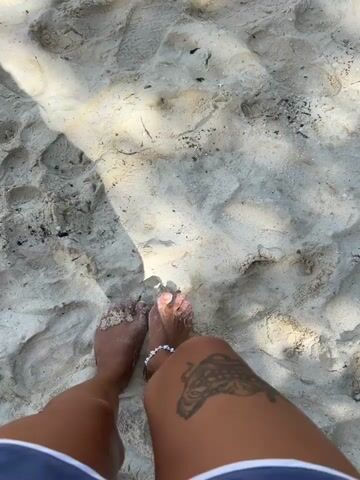 The video shows a pair of bare feet walking on a sandy beach. The sand is light in color and appears to be wet in some areas. There are footprints in the sand, indicating that others have walked there before. The feet are adorned with a delicate white anklet. The person's legs are visible, and a tattoo of what appears to be a mandala design is visible on the right thigh.

A shadow is cast across the sand, suggesting it is a sunny day. The light and shadows indicate it could be late morning or early afternoon. The scene is a beach, likely in a tropical location given the sand and overall bright atmosphere. The activity is simply walking on the beach. There is no visible text in the media. The overall mood seems relaxed and peaceful, consistent with a day at the beach. The location context of Ao Nang, Thailand, reinforces the visual cues of a tropical beach environment.