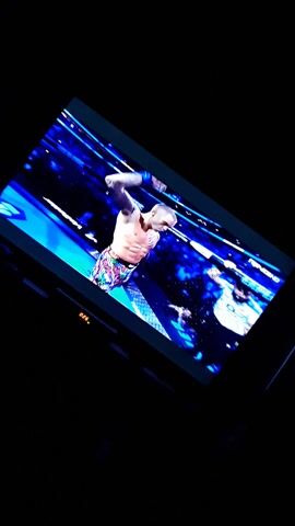 A man in patterned trunks is displayed on a television screen. The screen is tilted towards the viewer and surrounded by darkness. The man on the screen is flexing his arm and is in front of a blue backdrop. The words "CIRCO TEQUILA" are visible on the screen.