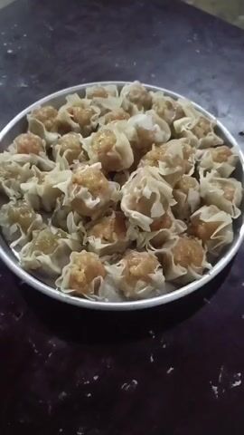 A plate of dim sum sits on a dark, textured surface. The dim sum are small, steamed dumplings with a light-colored wrapper and a visible filling. The plate is round and metallic. The background is dark and out of focus. The lighting is dim, and the video is shaky.