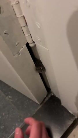 Here is a description of the video:
The video shows a person's hand near a partially open white door. A small, gray animal is wedged in the narrow space between the door and the frame. The person gently touches the animal with their finger. The animal seems to be stuck. The floor appears to be tiled in dark gray. The video is taken at a close angle to show the animal and the hand interacting.