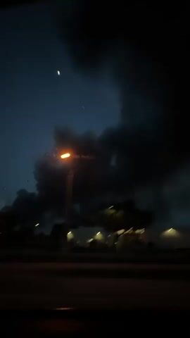 The video shows a view from inside a car at night. The camera pans across the sky, revealing dark, ominous storm clouds with faint glimpses of a twilight sky. Several streetlights illuminate buildings and trees in the foreground. There is little to no motion within the scene other than the camera movements.