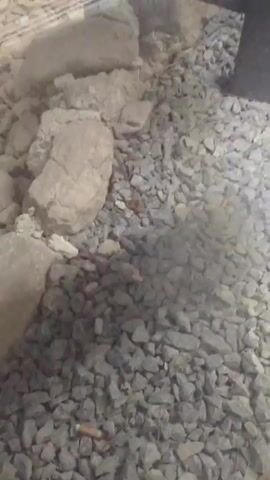 This media file is a video montage of four short clips. The first clip shows rocks and gravel. The second clip shows rocks and gravel through a glass enclosure. The third and fourth clips show a nighttime view of Polop, Spain. A bell tower with illuminated windows is prominent in the center of the frame, with lights of a town scattered on the hillside behind it and dark mountains silhouetted against the night sky. The overall impression is one of a scenic, possibly urban, landscape at night. There is no visible text in the media file.