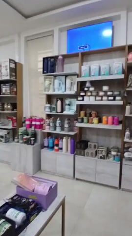 The video shows a brightly lit, well-organized retail store. The interior is clean and the walls are painted white. Shelves and display tables showcase a variety of items, including kitchen appliances, water bottles, mugs, and gift sets. The gift sets are arranged in black boxes on tables. A television is mounted on the wall in the back of the store. There are no people visible in the video. The camera slowly pans across the store.