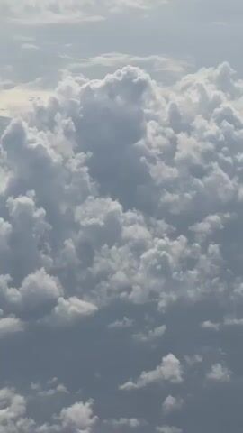 This is an aerial view of clouds. The clouds are white and gray, and they are scattered across a blue sky. The sun is shining through the clouds, creating a bright and airy atmosphere. The clouds appear to be in various stages of formation, with some appearing fluffy and cumulus-like, while others are more flat and stratiform. The lighting suggests it may be daytime, possibly late morning or afternoon.