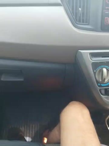 The video shows the interior of a car. The dashboard is visible, with vents and controls. A person's leg is visible in the lower right portion of the frame. The floor mats are visible beneath the leg.