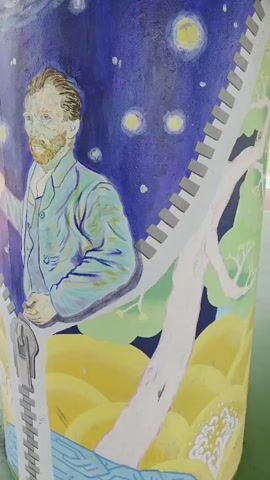 A mural painted on a cylindrical structure depicts a portrait of Vincent van Gogh against a backdrop of a starry night sky. A zipper graphic runs vertically down the structure, appearing to peel back the starry sky to reveal a landscape of yellow hills and a tree. Van Gogh is shown holding a bottle and pouring liquid into a glass. The video pans from left to right, showing the mural from different angles. The environment appears to be outdoors, with hints of a sports field or recreational area in the background.