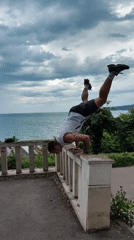 Man performs handstand push-ups on ocean-view concrete barrier