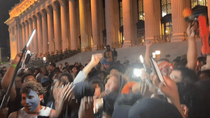 Young crowd gathers at night near columned NYC building