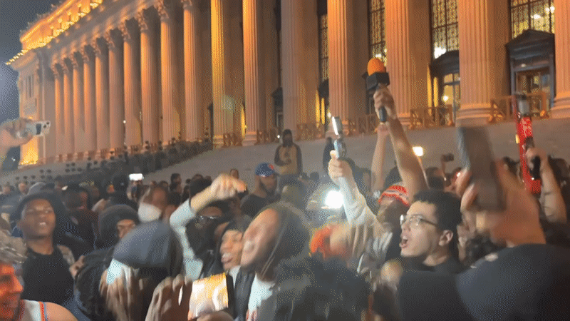Young crowd gathers at night near columned NYC building