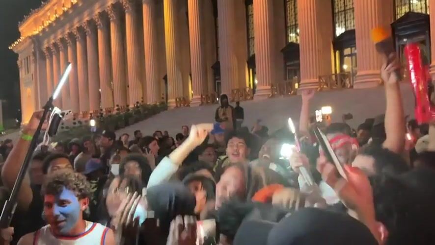 Young crowd gathers at night near columned NYC building