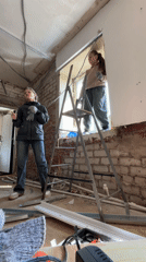 Two women perform window construction work in unfinished room