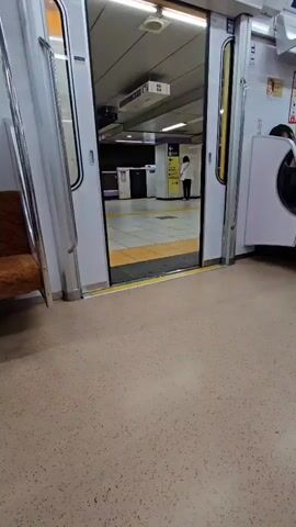 From inside a train, the doors are seen closing. The train interior is white with a yellow stripe on the floor where the doors slide into the train. A brown upholstered seat is visible to the left. The camera faces the closing doors, then tilts upward to show the white wall of the train.
